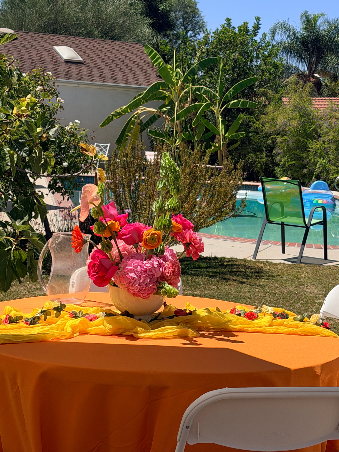 Poolside guest table with pink hydrangea and ranunculus centerpiece on a marigold runner