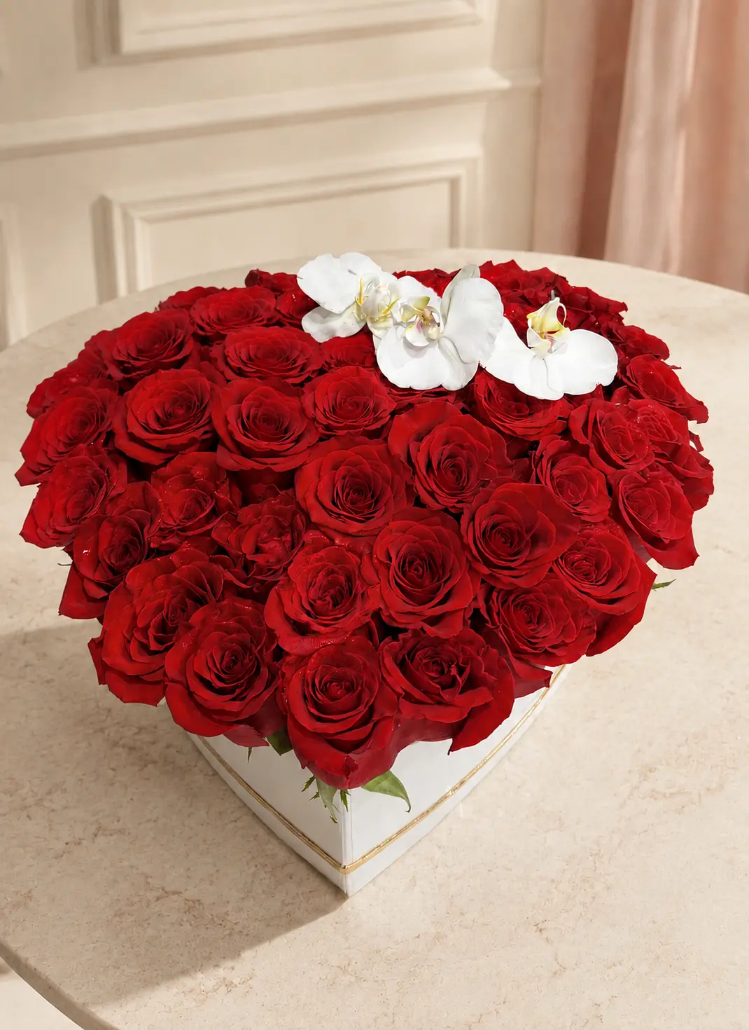 Heart-shaped arrangement of premium red roses accented with white orchids in a white keepsake box with gold trim
