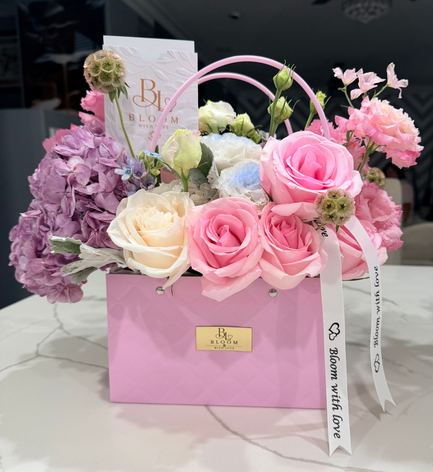 Blushing Love arrangement of premium roses, hydrangeas and seasonal florals in a pink handbag-style container with Bloom with Love ribbon