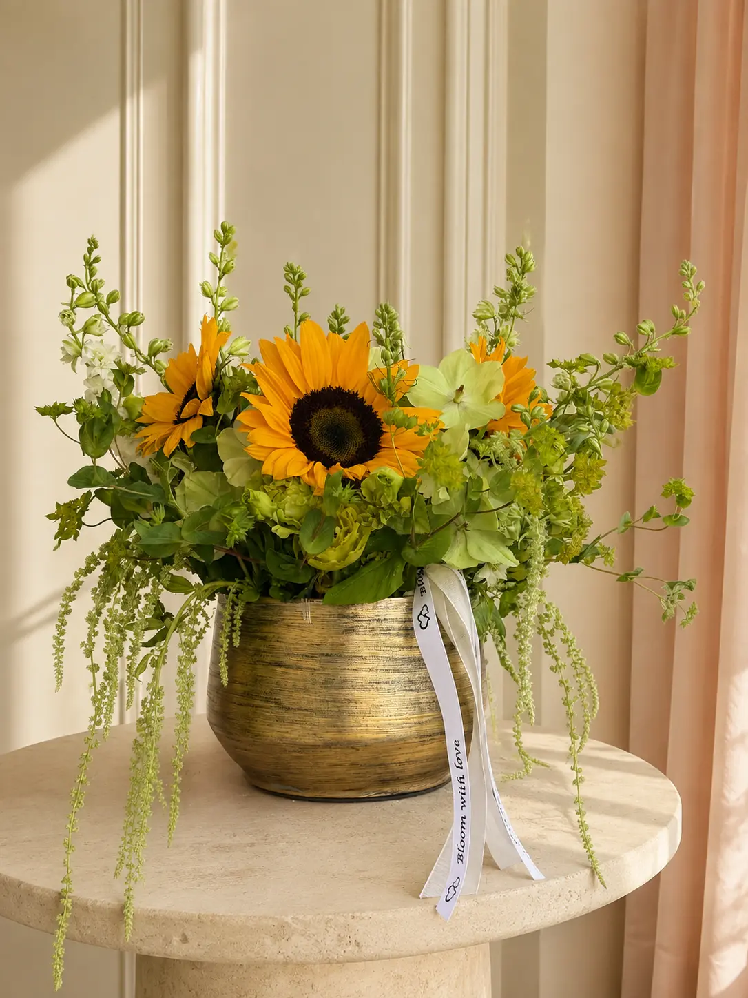 Sunshine Blooms arrangement of sunflowers, green hydrangea, bells of Ireland and hanging amaranthus in a gold vessel