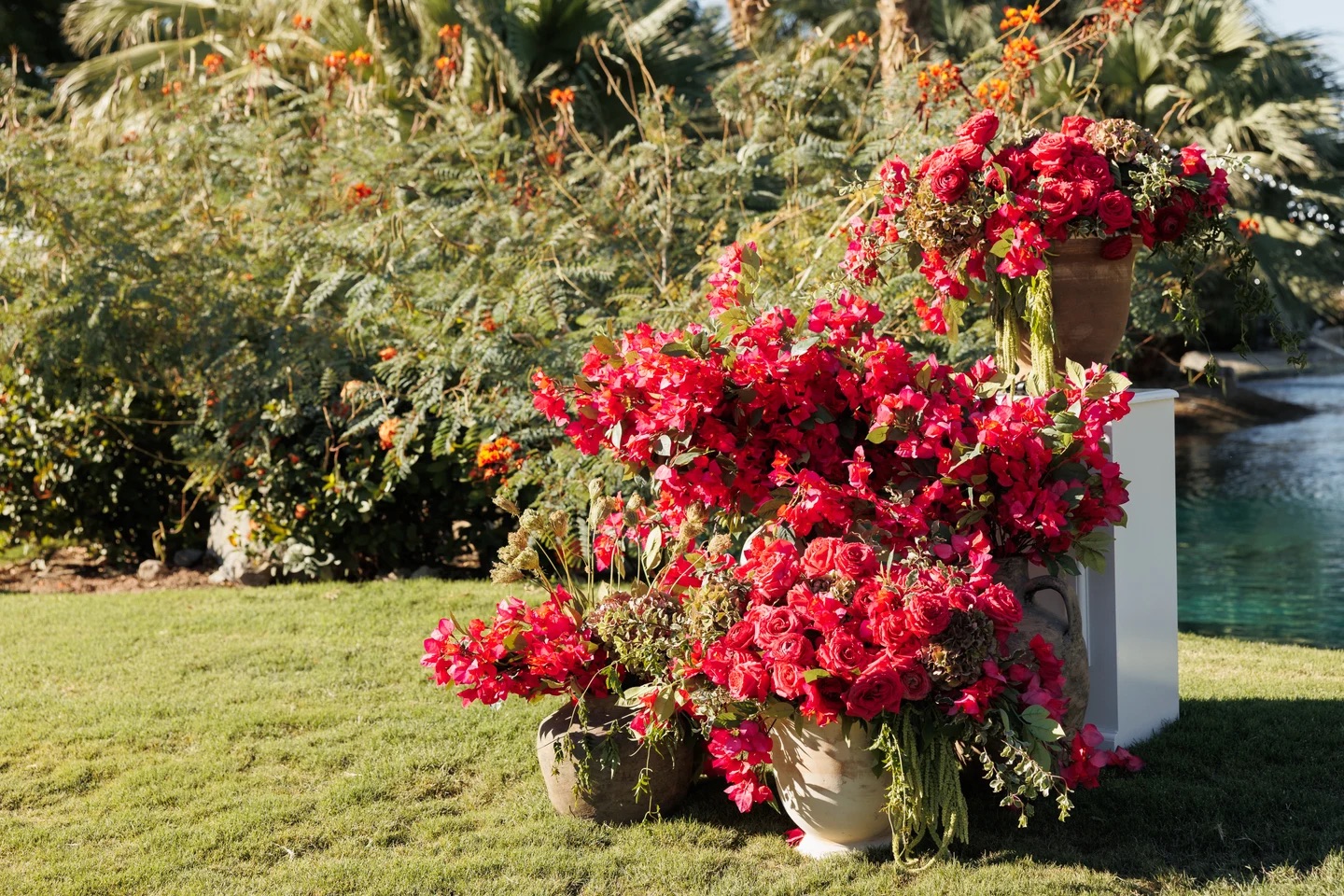 Ground floral installation of red roses and bougainvillea in terracotta urns beside a resort lake
