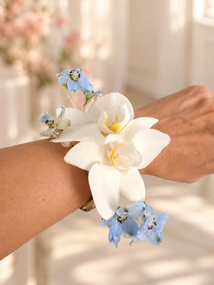 White orchid wrist corsage with delicate blue flowers on a gold cuff