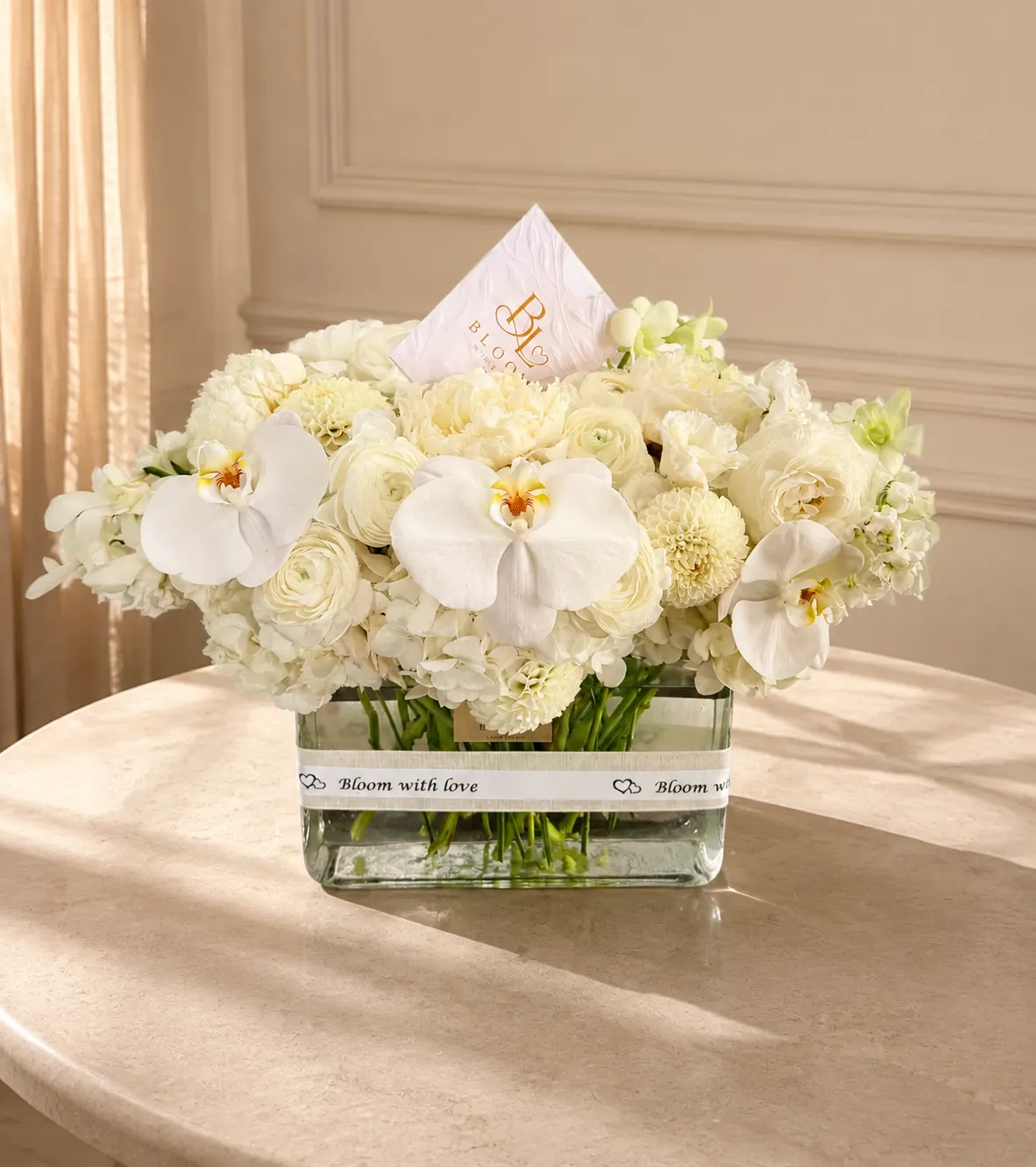 Orchid and Ivory Luxe arrangement with three white phalaenopsis orchids, ranunculus, dahlias and hydrangeas in a clear glass vase