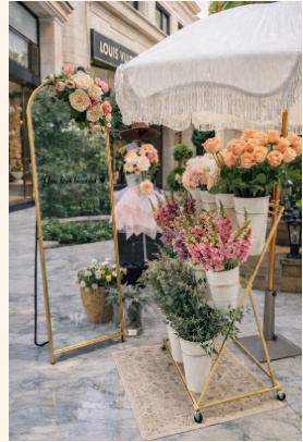 The Bloom With Love bloom bar cart styled with buckets of garden roses, snapdragons and eucalyptus beside a gold-framed mirror and fringed umbrella at an event