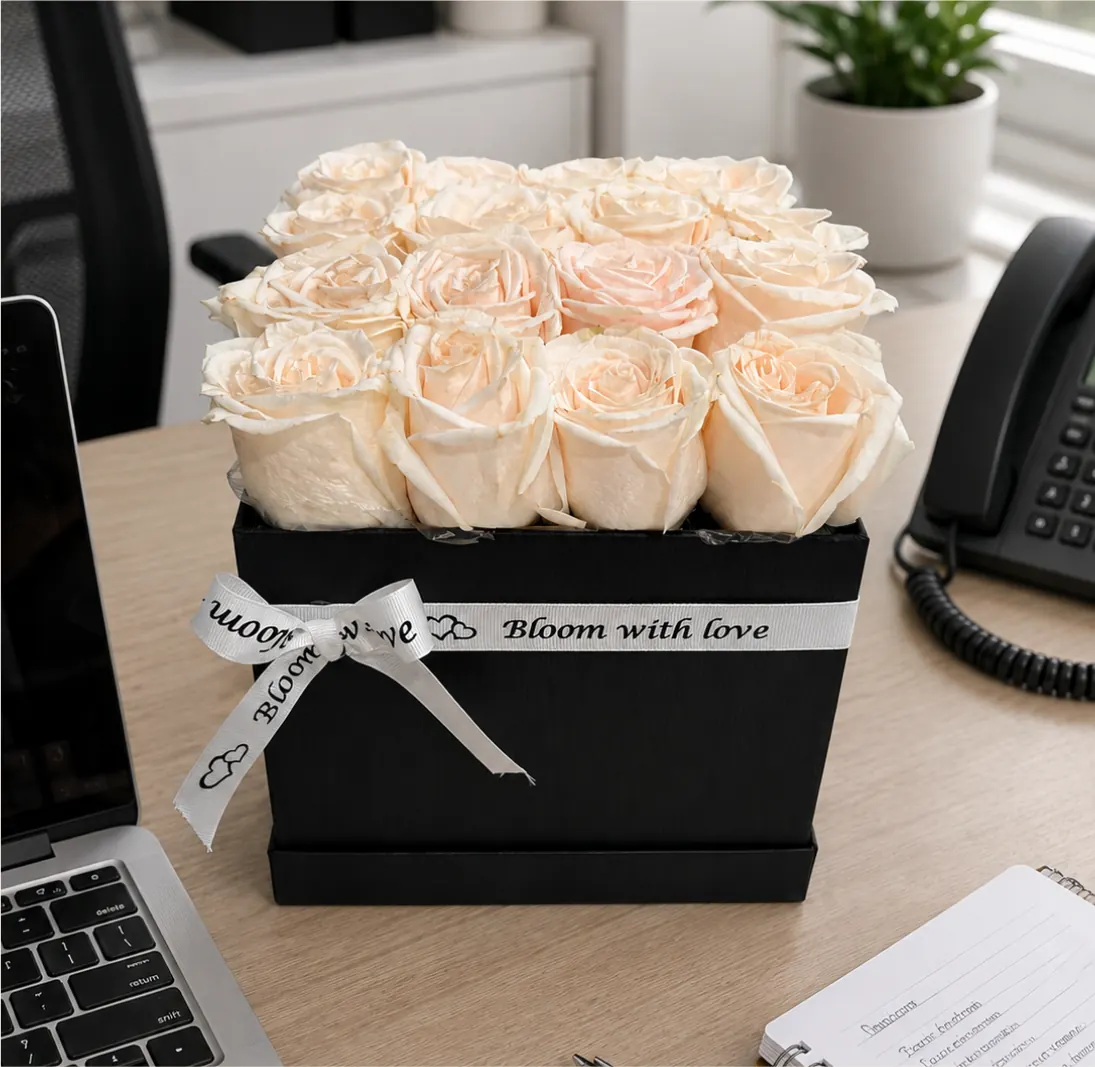 Black keepsake box filled with pale peach roses tied with a Bloom With Love ribbon, styled on an office desk beside a laptop