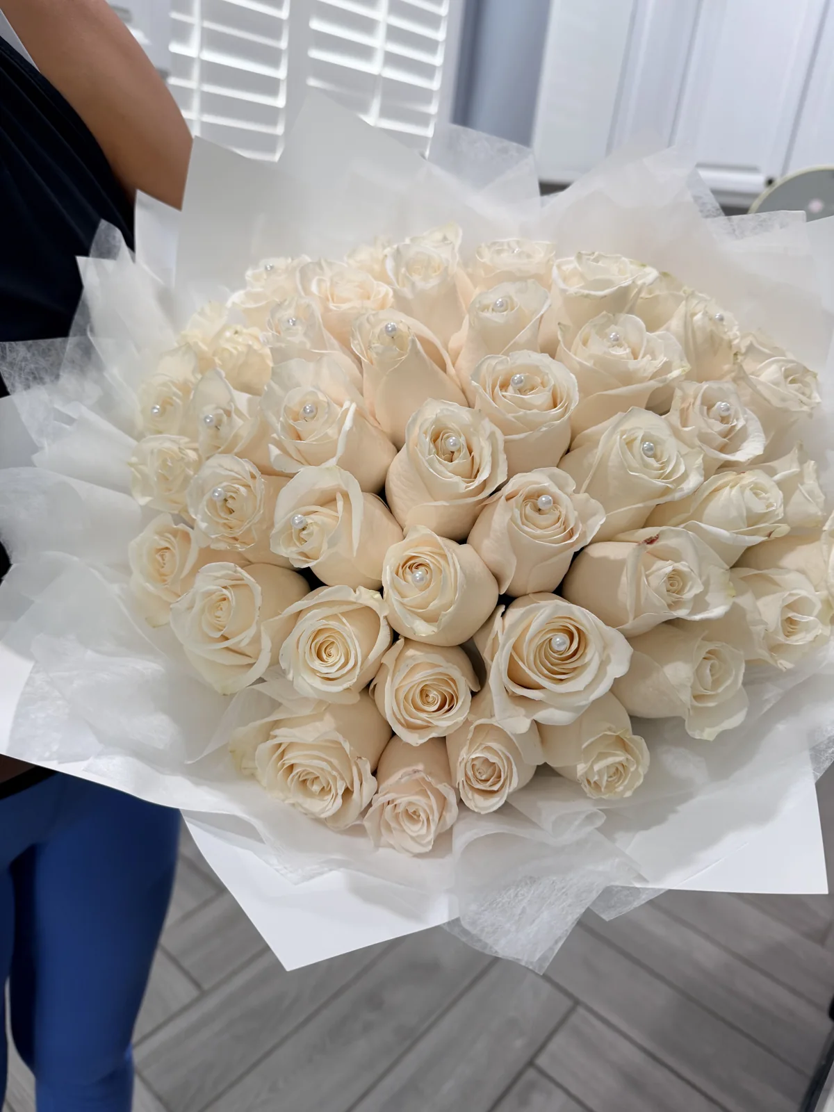 Hand-held bouquet of ivory roses with pearl accents and translucent white wrapping