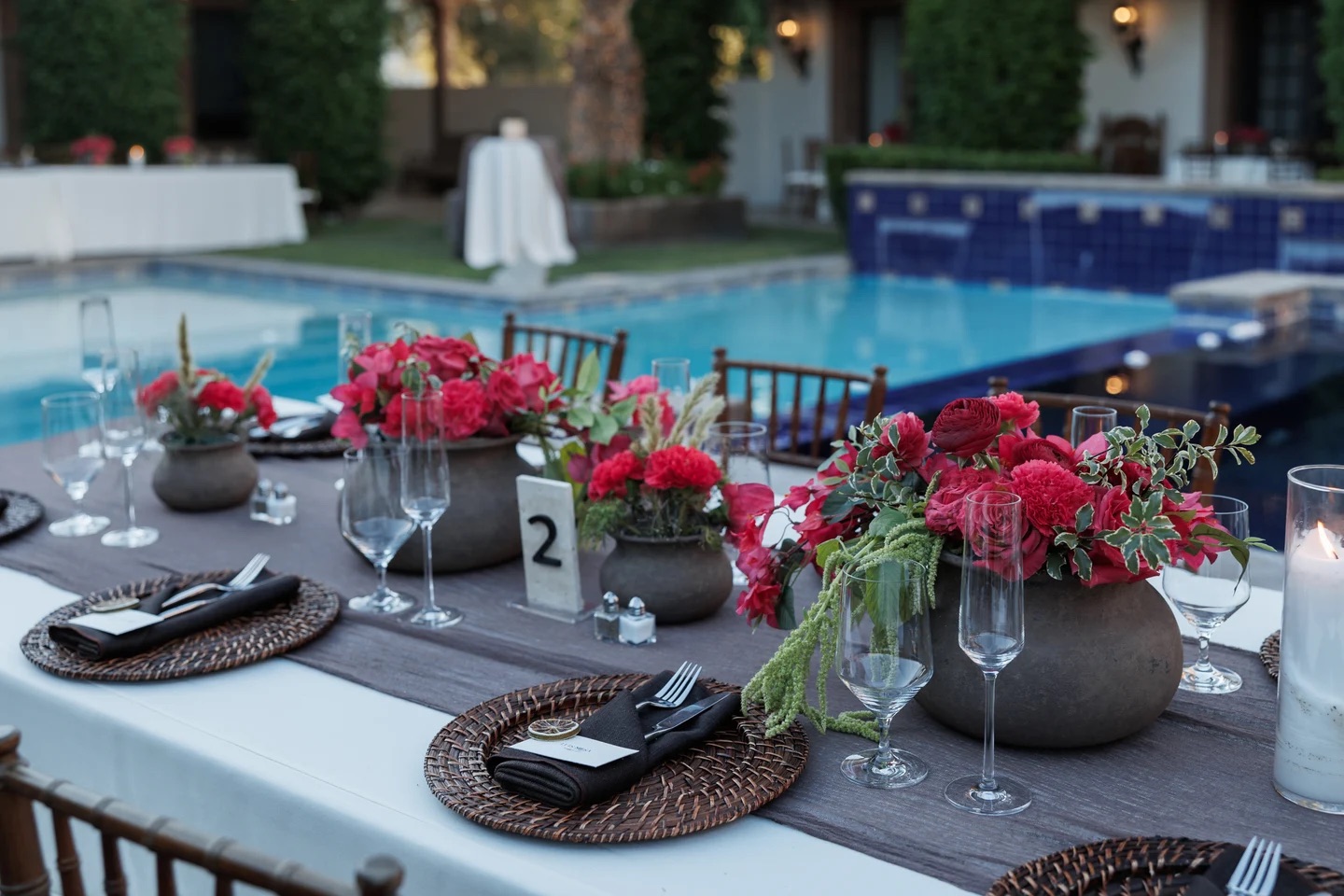 Poolside reception tablescape with crimson rose and carnation centerpieces in stone vessels