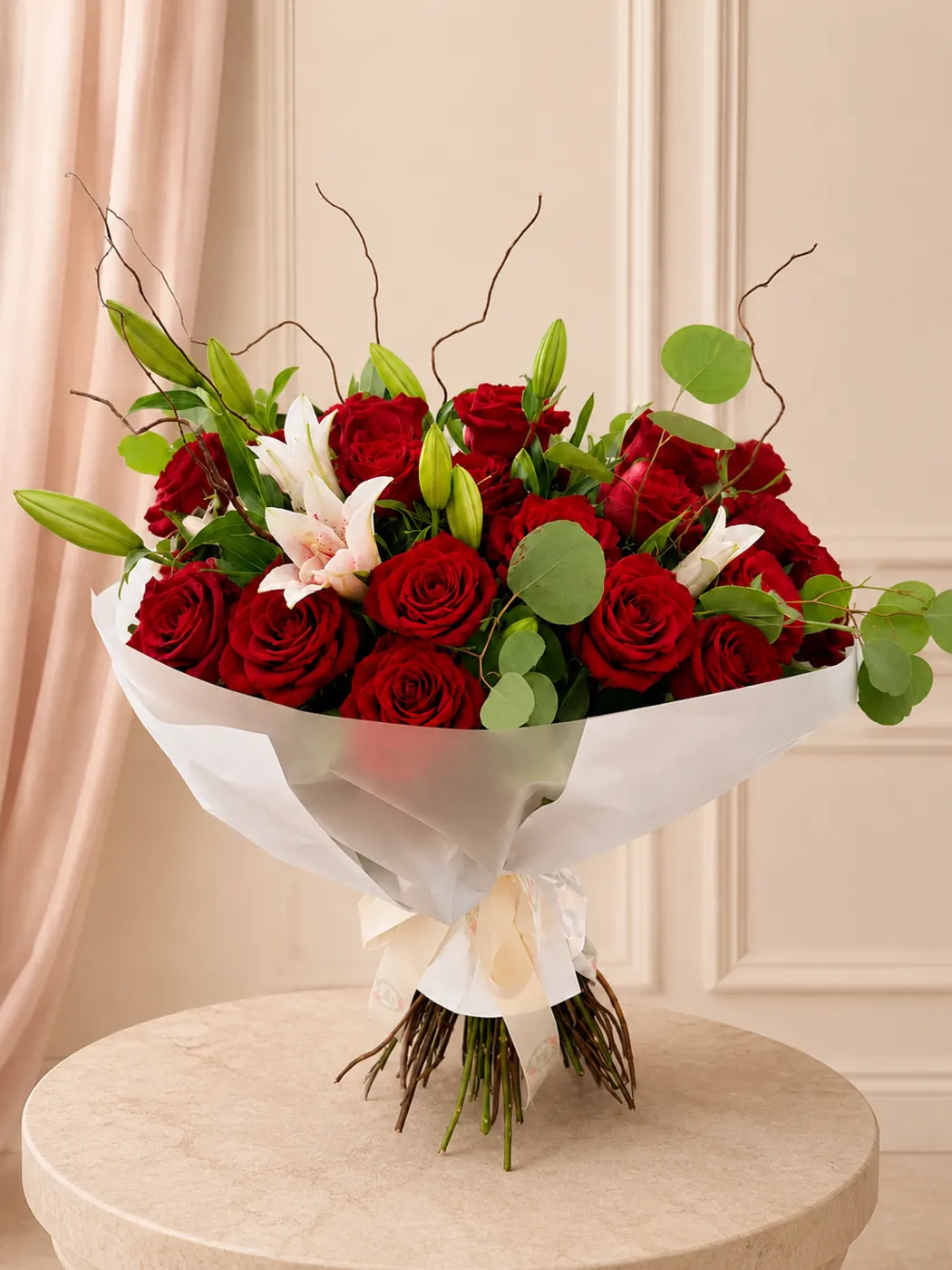 Garden-style bouquet of premium red roses, white and blush lilies, eucalyptus and sculptural branches in soft white wrapping