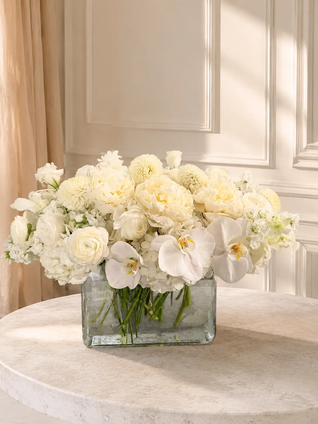 Grand Ivory oversized arrangement with white phalaenopsis orchids, peonies, ranunculus, dahlias and hydrangeas in a wide glass vase