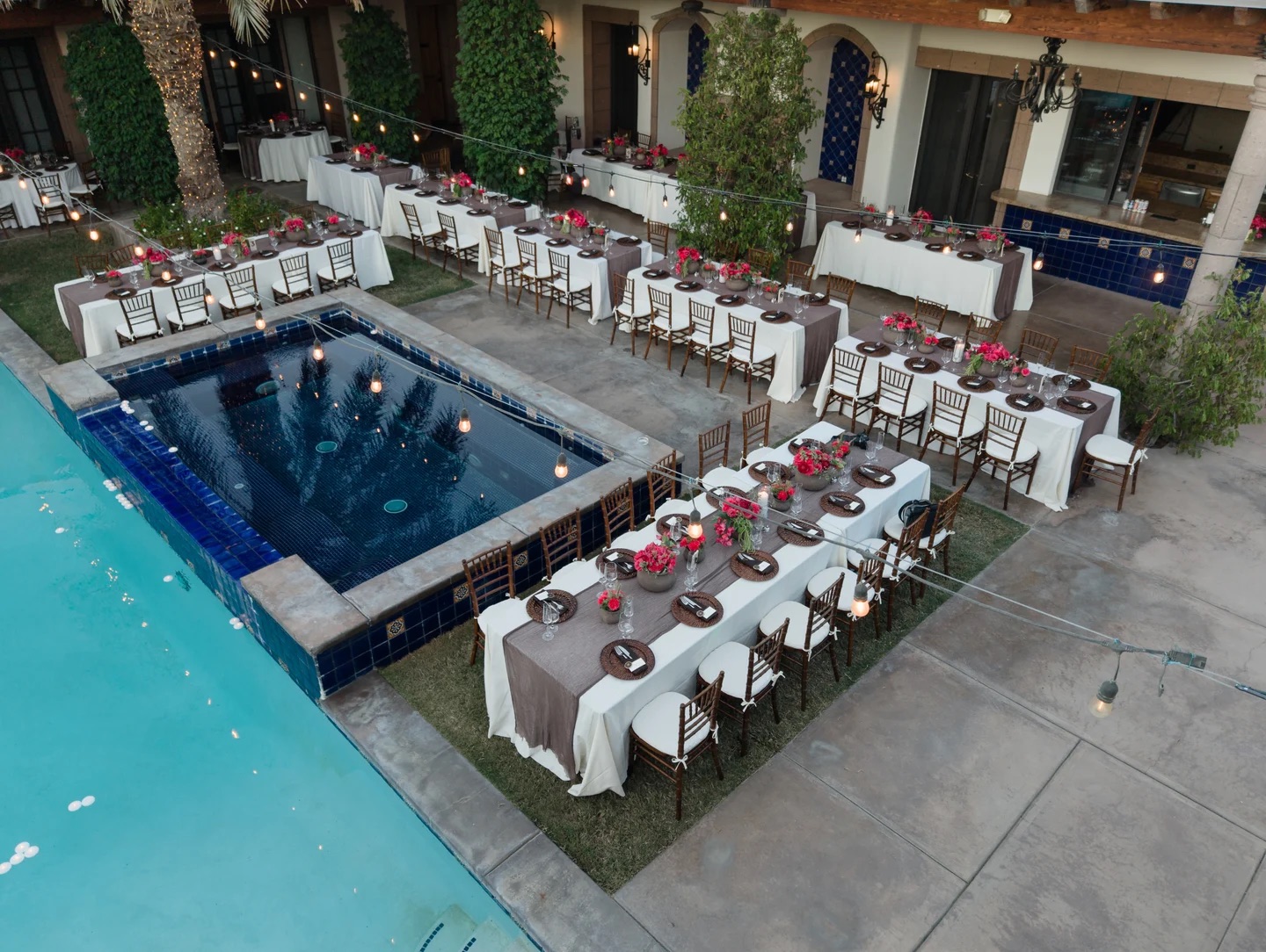 Aerial view of a poolside wedding reception with long tables and red floral centerpieces