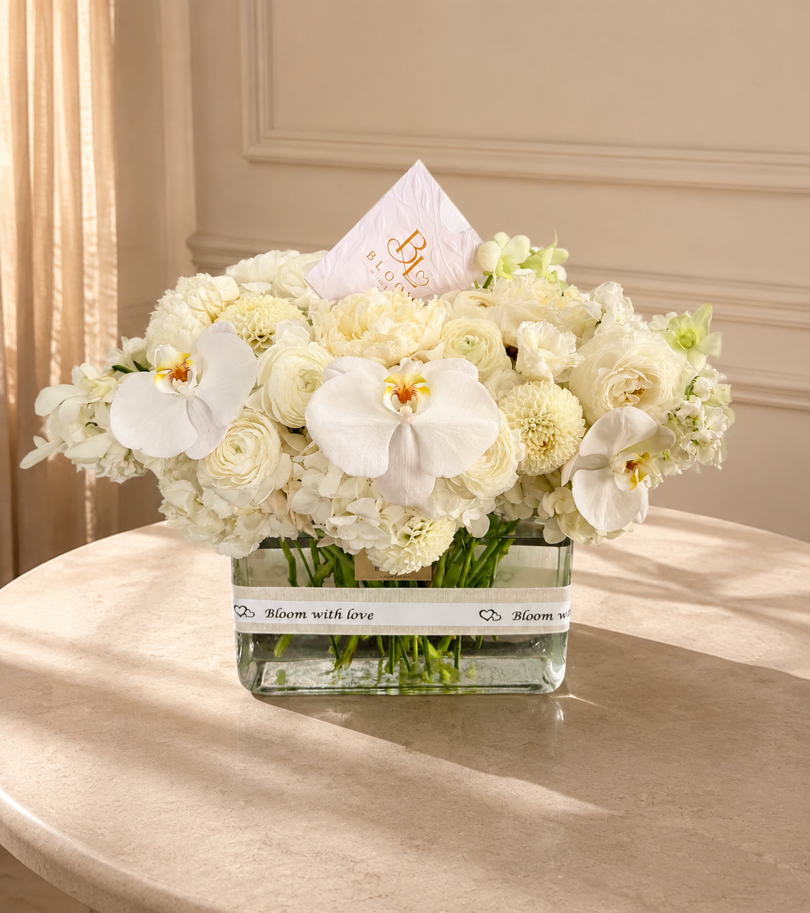 Orchid and Ivory Luxe arrangement with three white phalaenopsis orchids, ranunculus, dahlias and hydrangeas in a clear glass vase