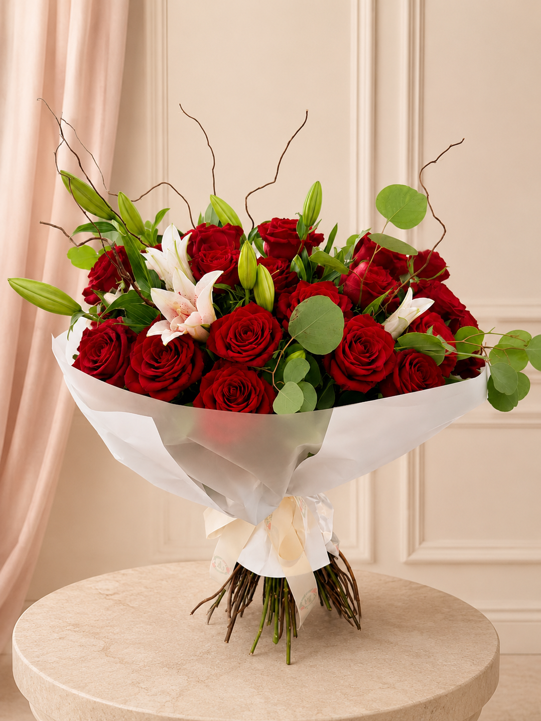 Garden-style bouquet of premium red roses, white and blush lilies, eucalyptus and sculptural branches in soft white wrapping