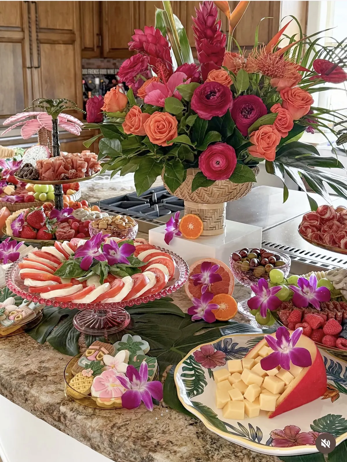 Tropical arrangement in a woven pedestal vessel above a colorful grazing table