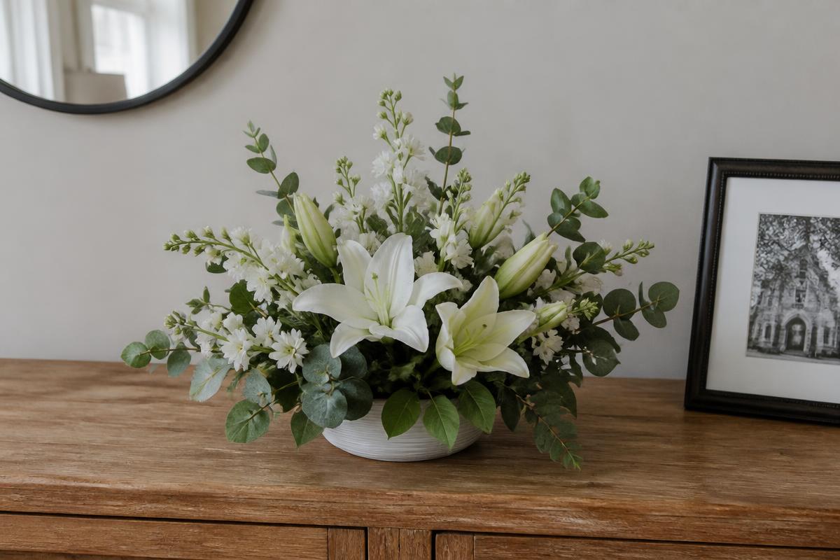 White lily and stock sympathy arrangement in a low ceramic vessel on a console table