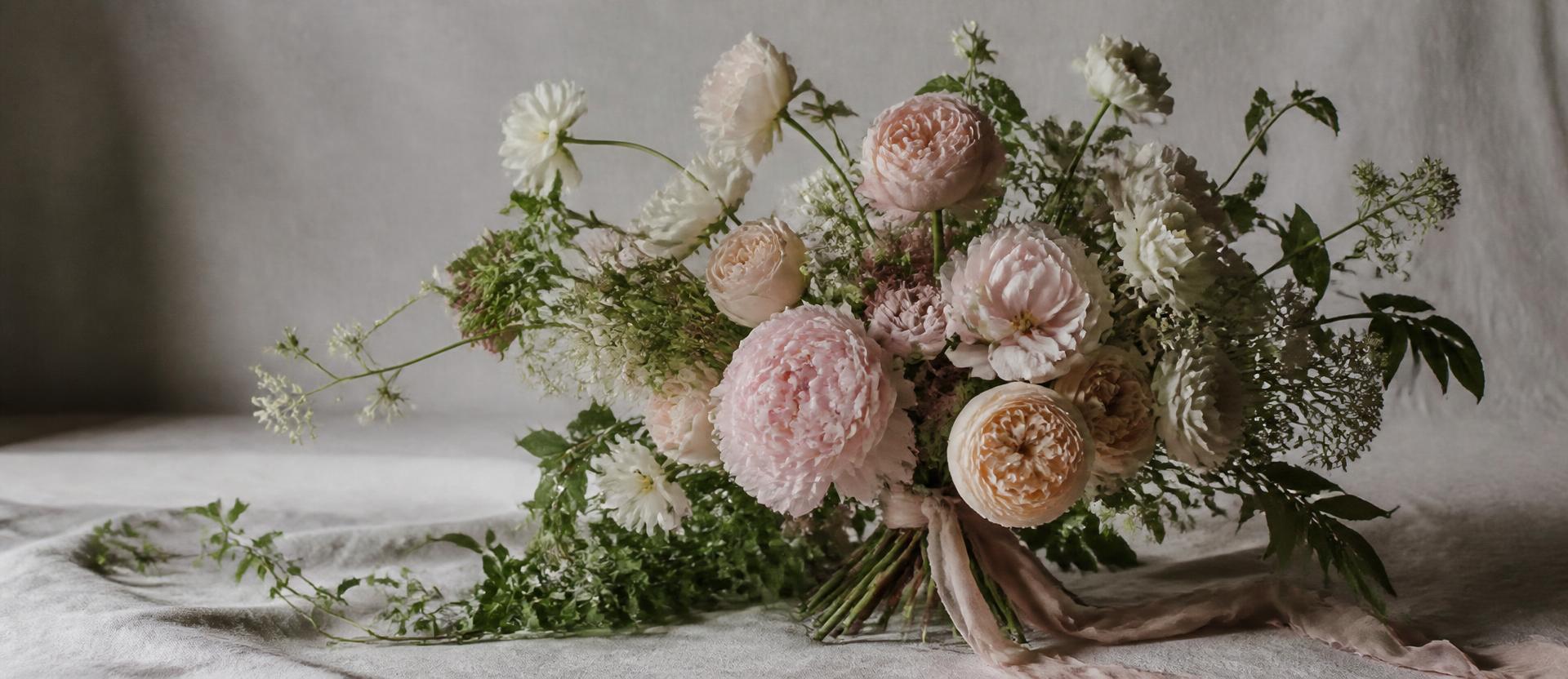 Hand-tied bouquet of blush peonies and garden roses on cream linen